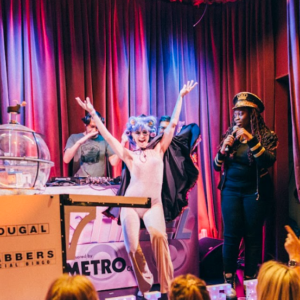 Energetic performance at an event with a DJ, dancers, and audience in colorful lighting.