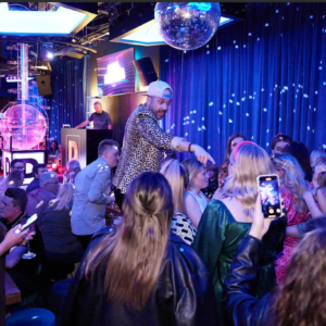 Crowd enjoying a lively nightlife scene with a DJ, disco ball, and party atmosphere.