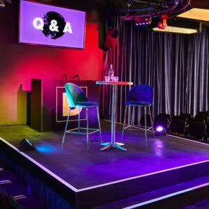 Q&A stage setup with colorful lighting, empty chairs, and a modern design backdrop.